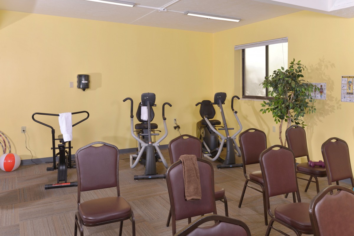 A small gym with exercise equipment and chairs arranged in a room with yellow walls.