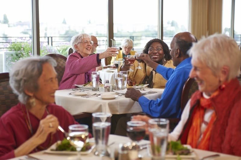 A group of elderly friends enjoying a meal together, raising their glasses in celebration at a restaurant.