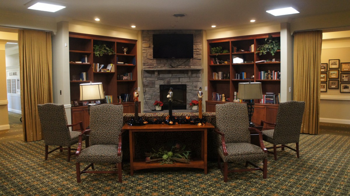 A cozy library with comfortable chairs and a fireplace surrounded by bookshelves.