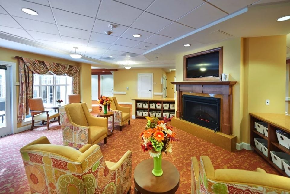 A cozy living room with comfortable seating arranged around a fireplace and television, decorated with floral arrangements and warm lighting.