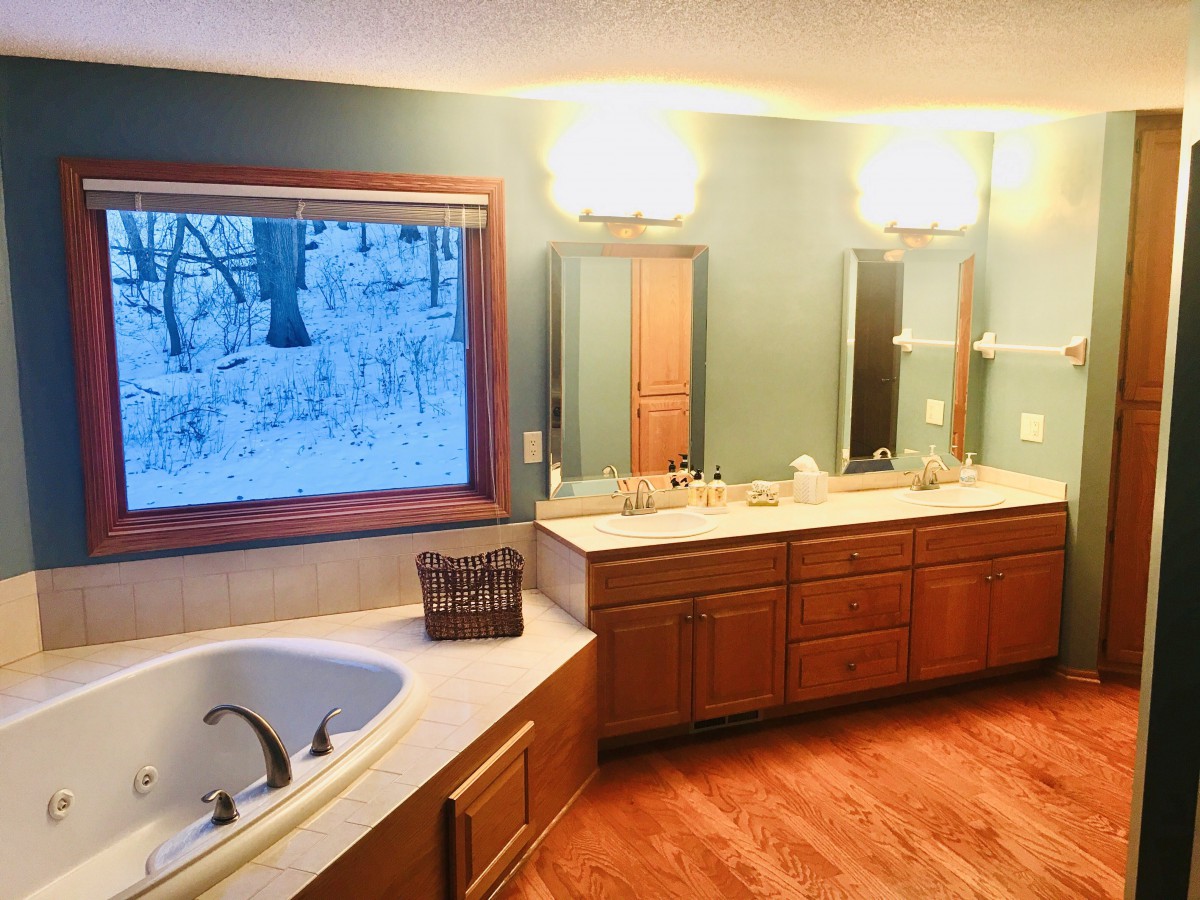A spacious bathroom featuring a large bathtub, double sinks, and wooden cabinetry with a snowy outdoor view.