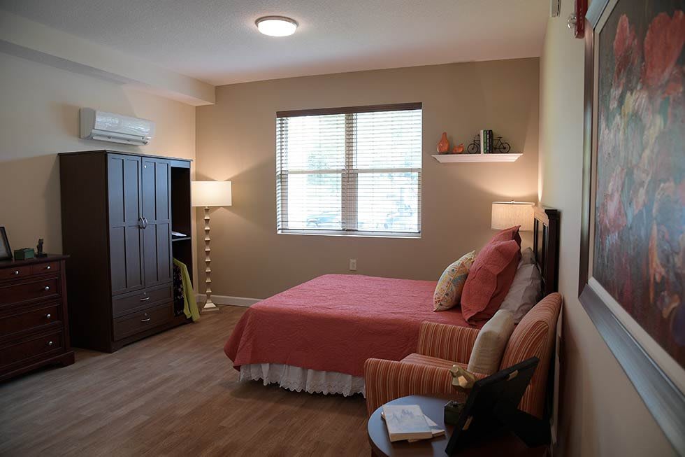 A cozy bedroom with a neatly made bed, armchair, and ambient lighting, featuring warm tones and minimalistic decor.