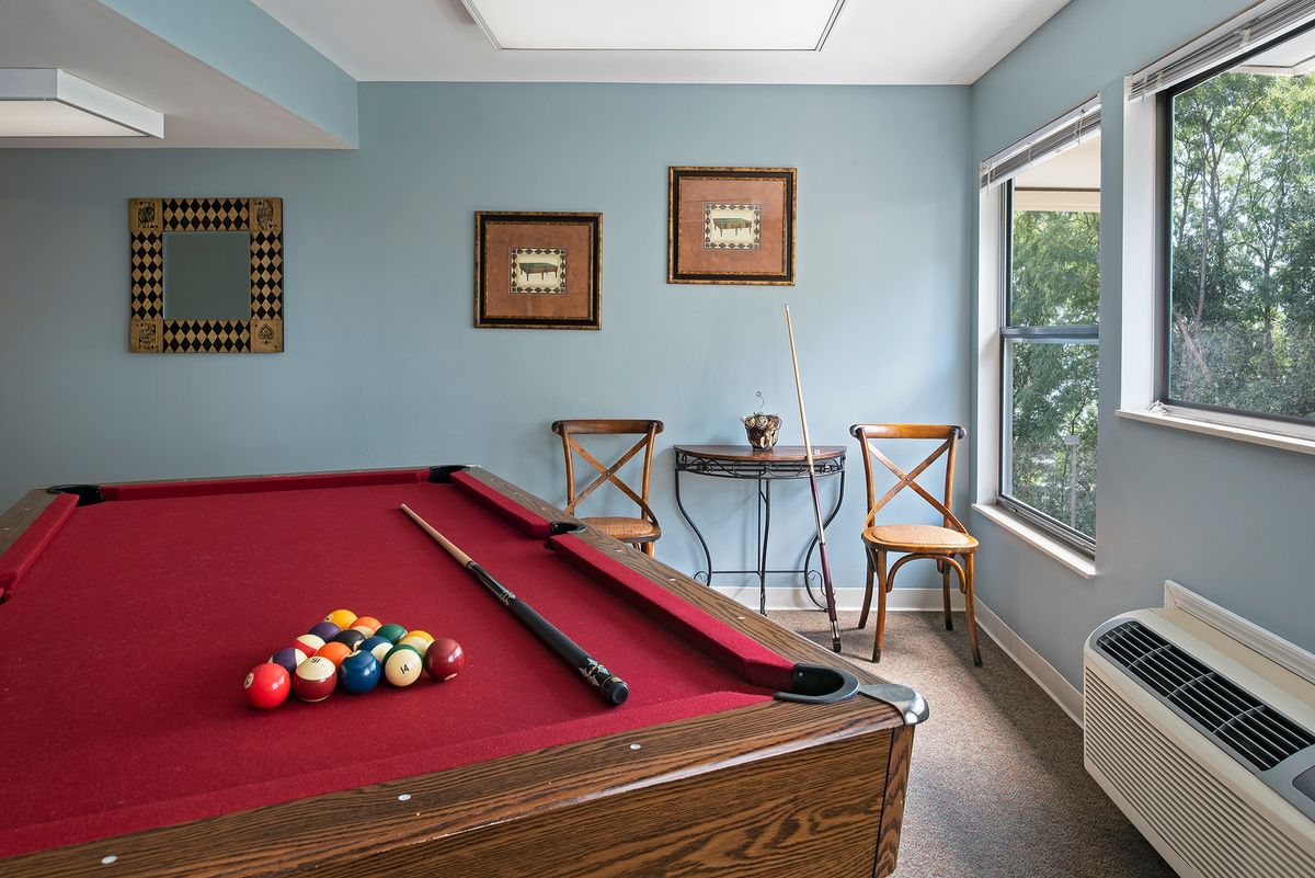 A cozy game room featuring a red-felt pool table beside a window and seating area.
