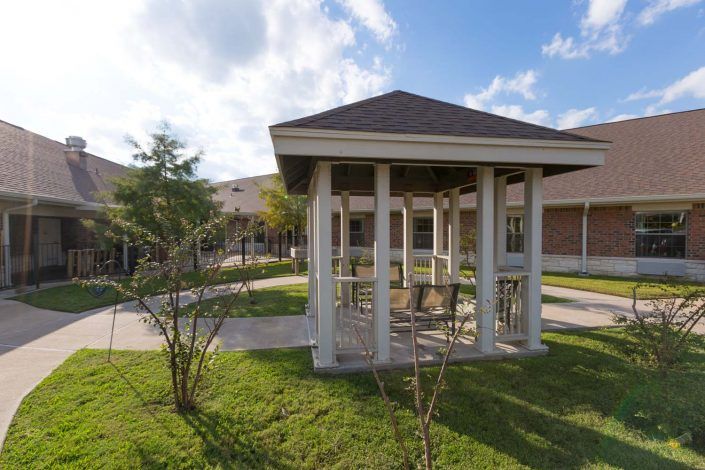 An outdoor gazebo on a grassy lawn near a building under a clear blue sky.