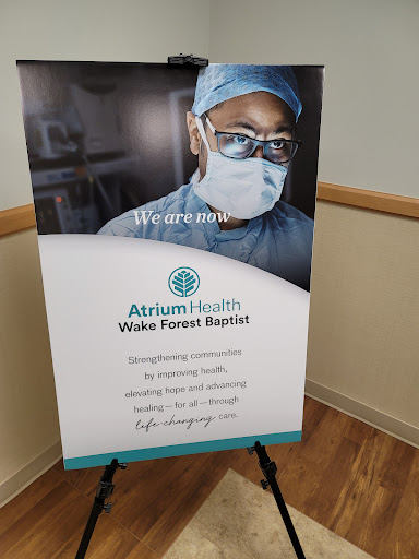 A promotional sign for Atrium Health Wake Forest Baptist featuring a medical professional in safety gear.