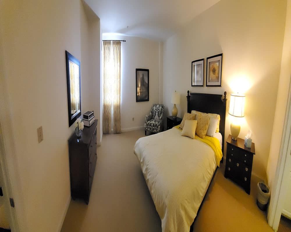 A cozy bedroom with a neatly made bed, warm lighting, and framed artwork on the walls.