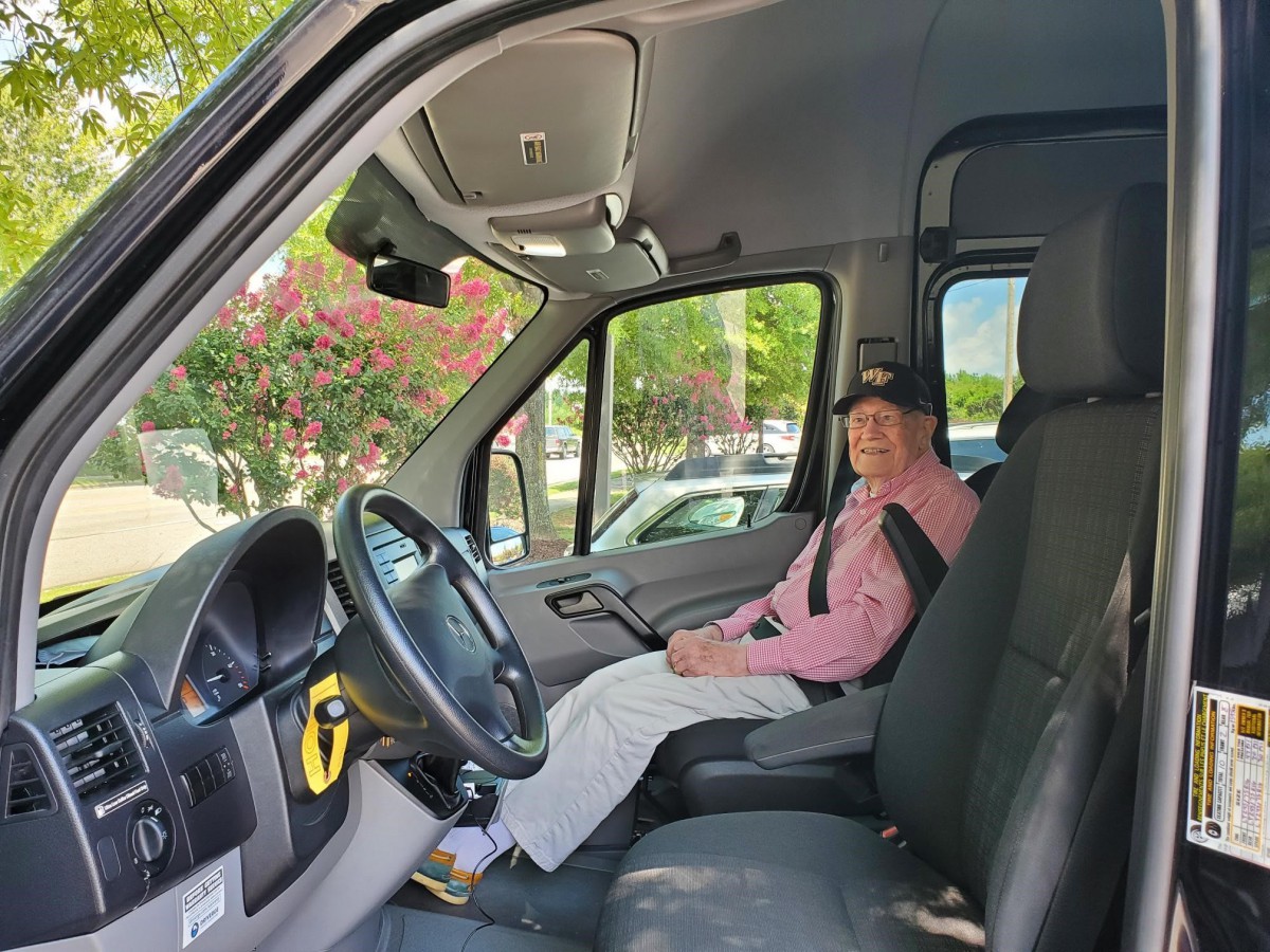 A person sits in the driver's seat of a parked van, wearing a seatbelt.
