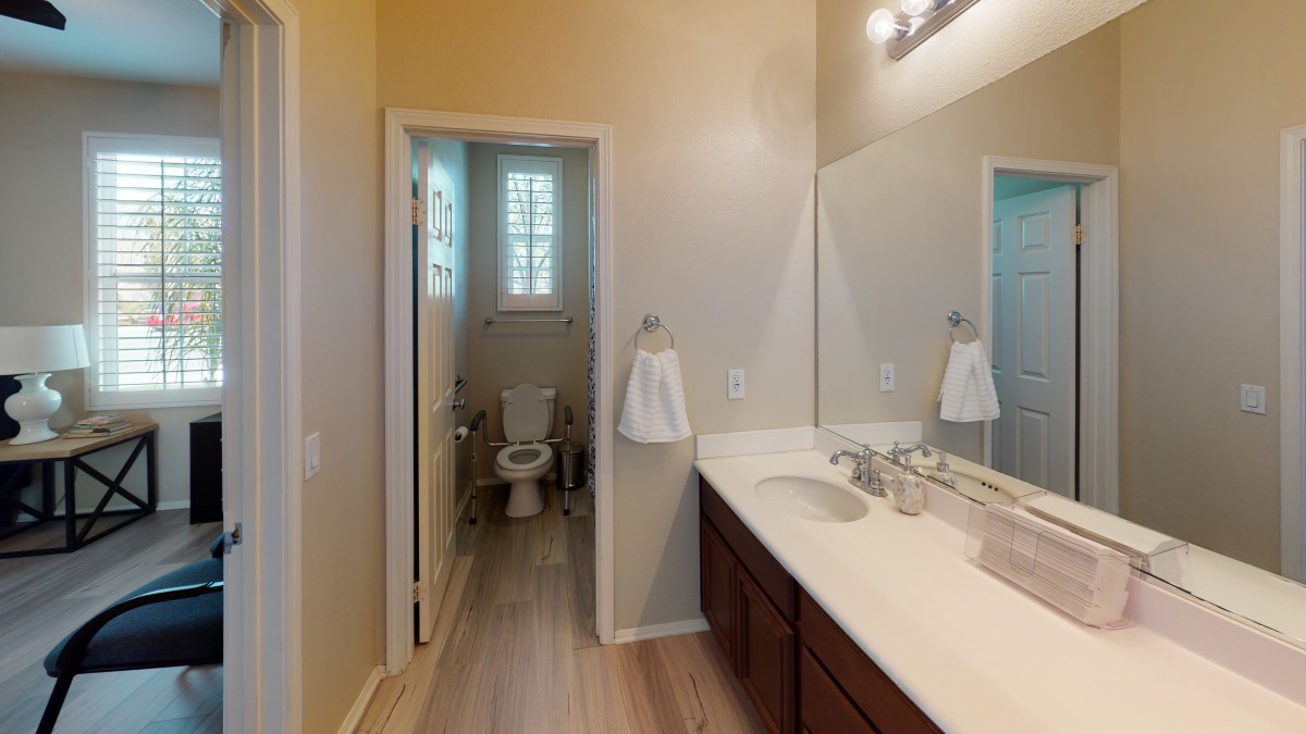 A modern bathroom with a large mirror, sink, and adjacent toilet area.