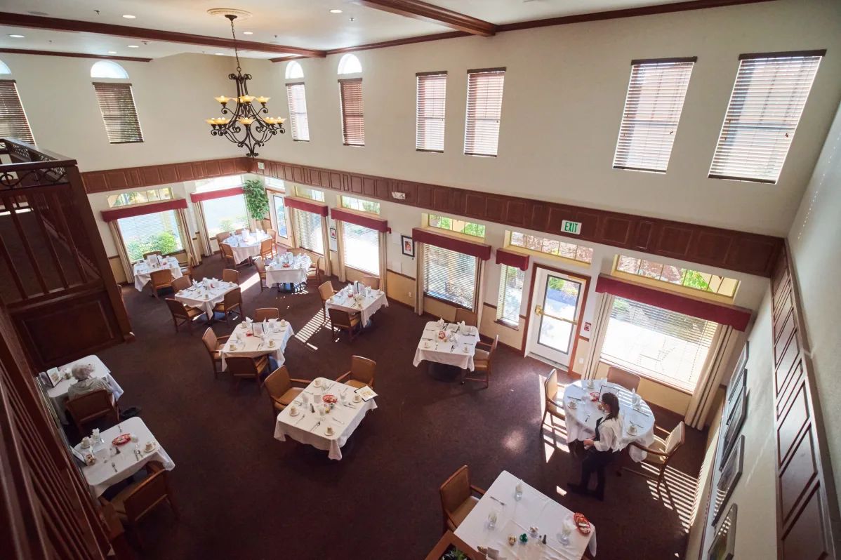 An empty restaurant dining room with neatly arranged tables and chairs, illuminated by natural light from the windows.
