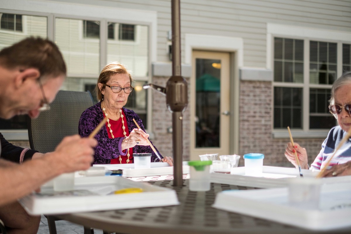 A group of elderly individuals engaged in painting crafts outdoors.