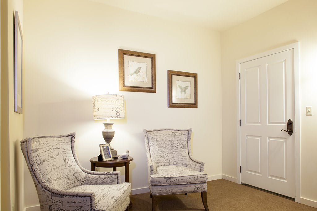 A cozy corner featuring two upholstered chairs, a small side table with a lamp, and framed artwork on the wall.
