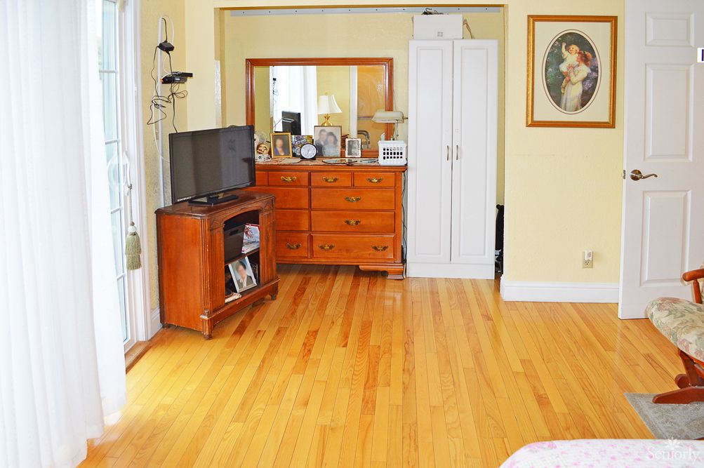 A cozy bedroom with hardwood floors, featuring a dresser with a mirror, a TV stand, and a closet.
