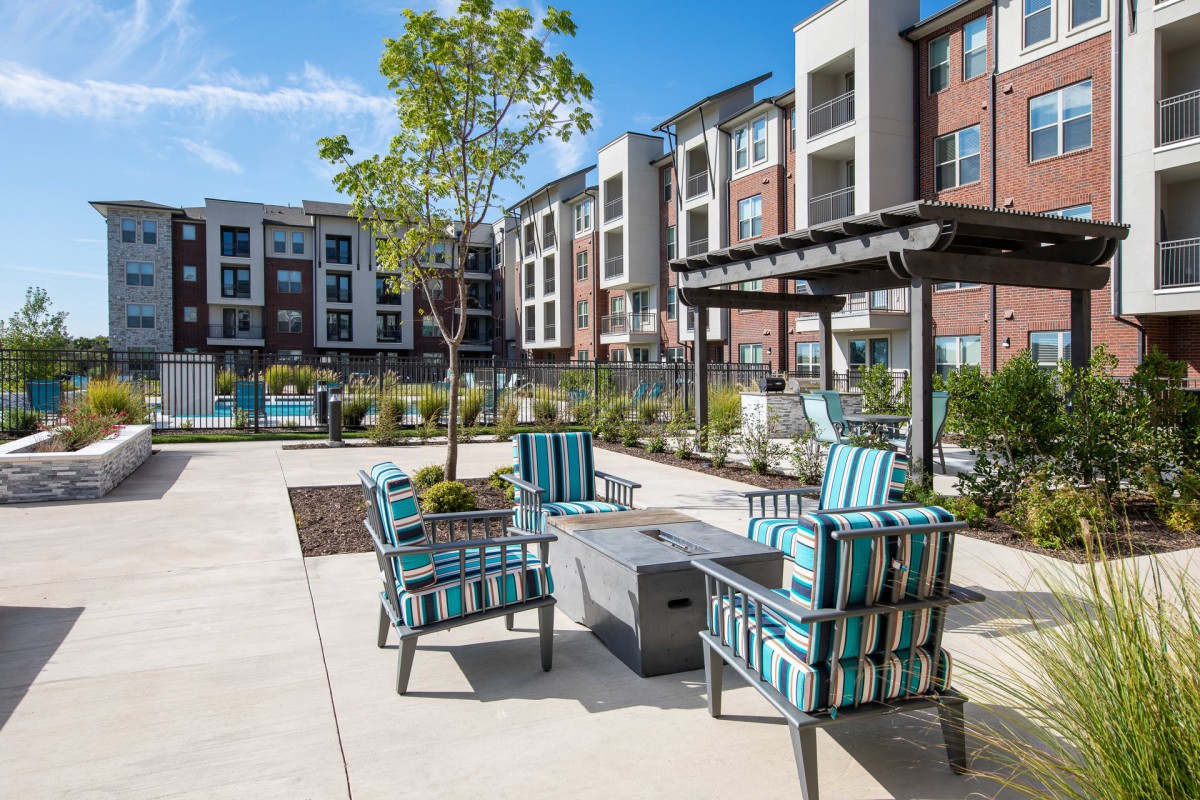 A modern apartment complex with outdoor seating and landscaped surroundings on a sunny day.