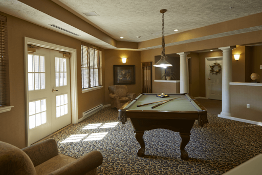 A cozy gaming room featuring a pool table, comfortable seating, and warm brown tones.