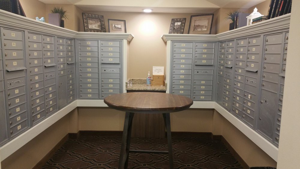 A quiet mailroom with rows of secure mailboxes and a central table for sorting letters.
