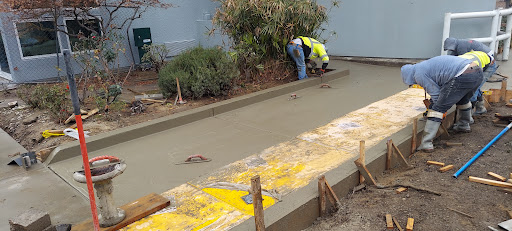 A worker is pouring and smoothing concrete in a landscaping area.