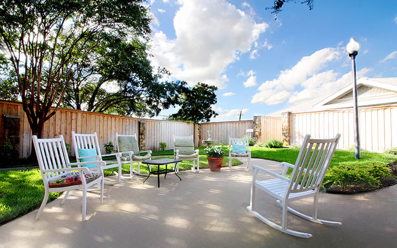 A sunny patio with white rocking chairs and a small garden area.