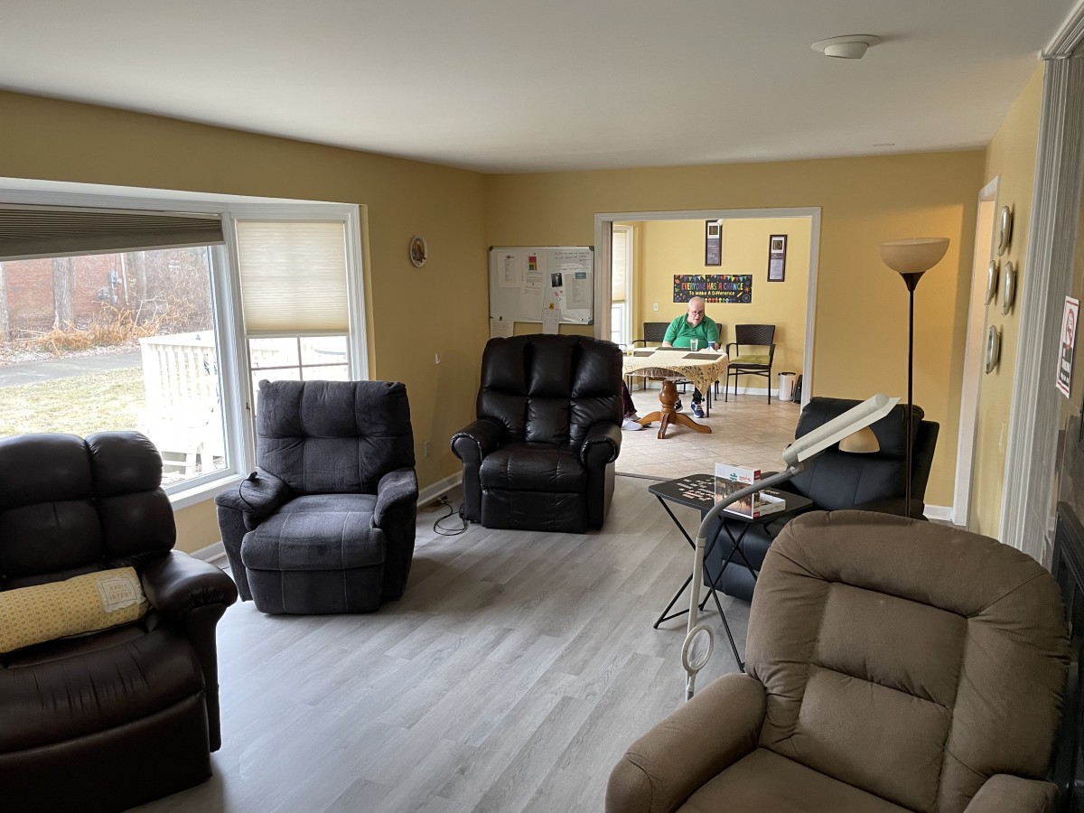 A cozy living room featuring multiple recliner chairs and a large window, with a view into the adjoining room.