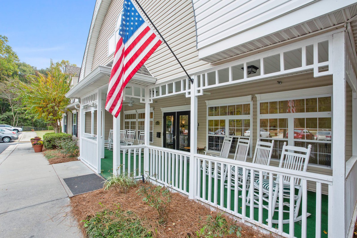 A charming house with a porch featuring rocking chairs and an American flag.