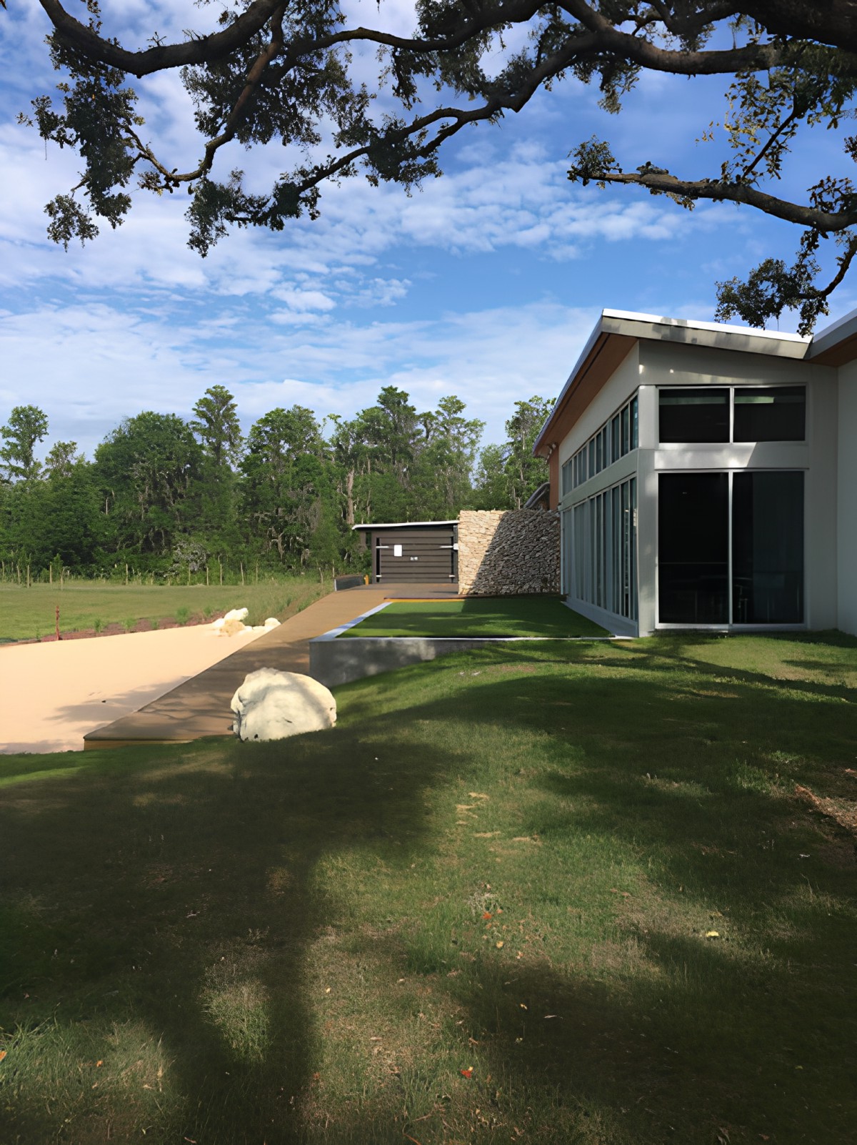 A modern building with large glass windows surrounded by a lawn and trees on a sunny day.