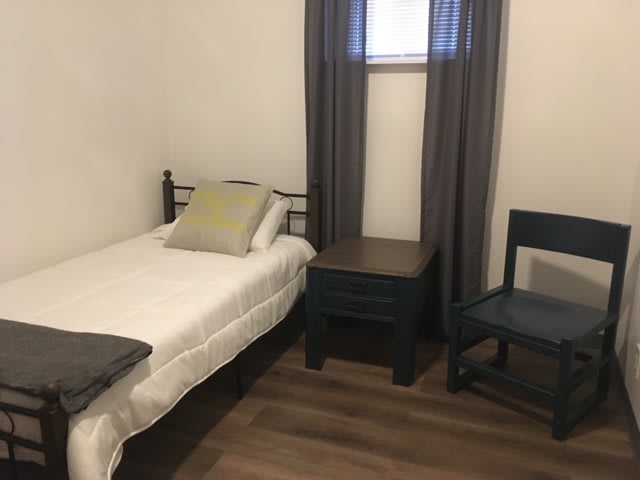 A minimalist bedroom with a single bed, nightstand, and chair.