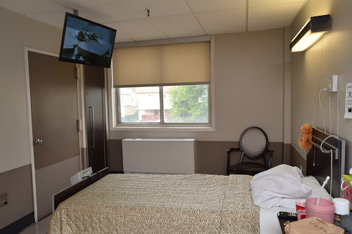 A view of a hospital room featuring an unmade bed, a television, and a window.
