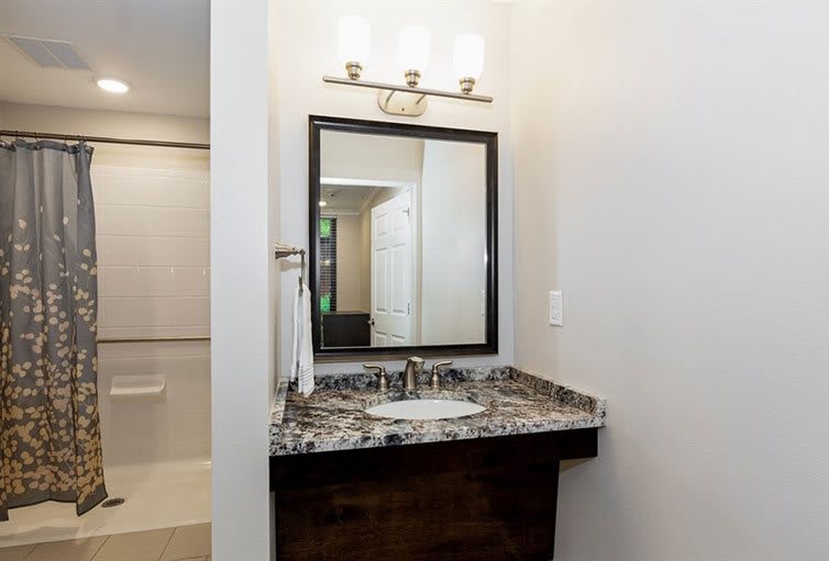 A modern bathroom vanity with a marble countertop and mirror, complemented by overhead lighting.