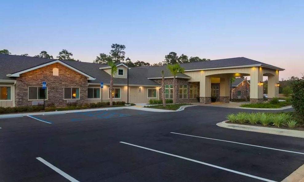 A modern building with a large parking lot and surrounding landscape at dusk.