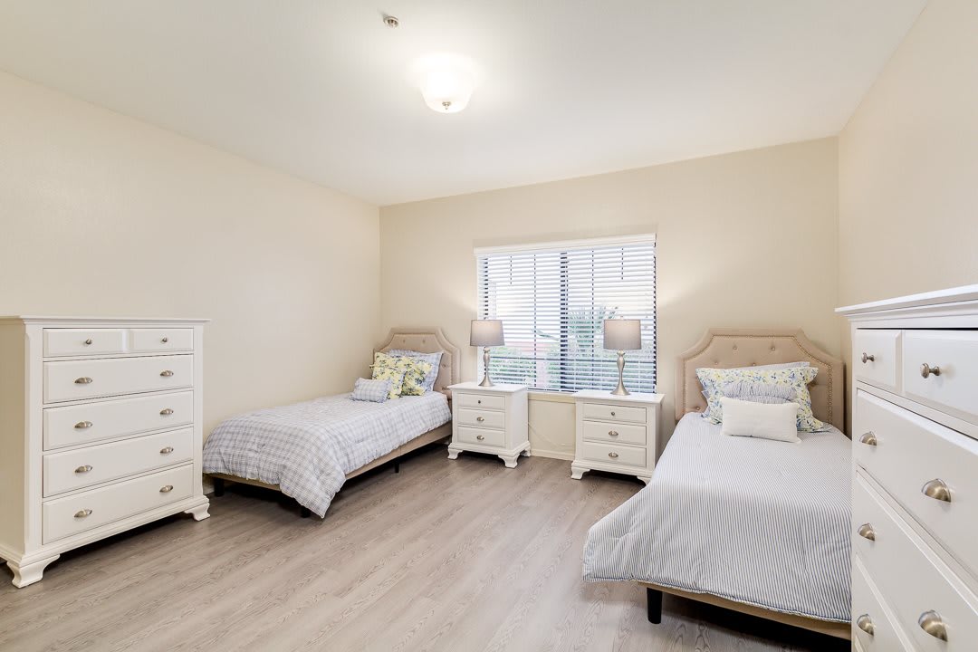 A bright and minimalist bedroom featuring two single beds, two nightstands with lamps, and dressers.