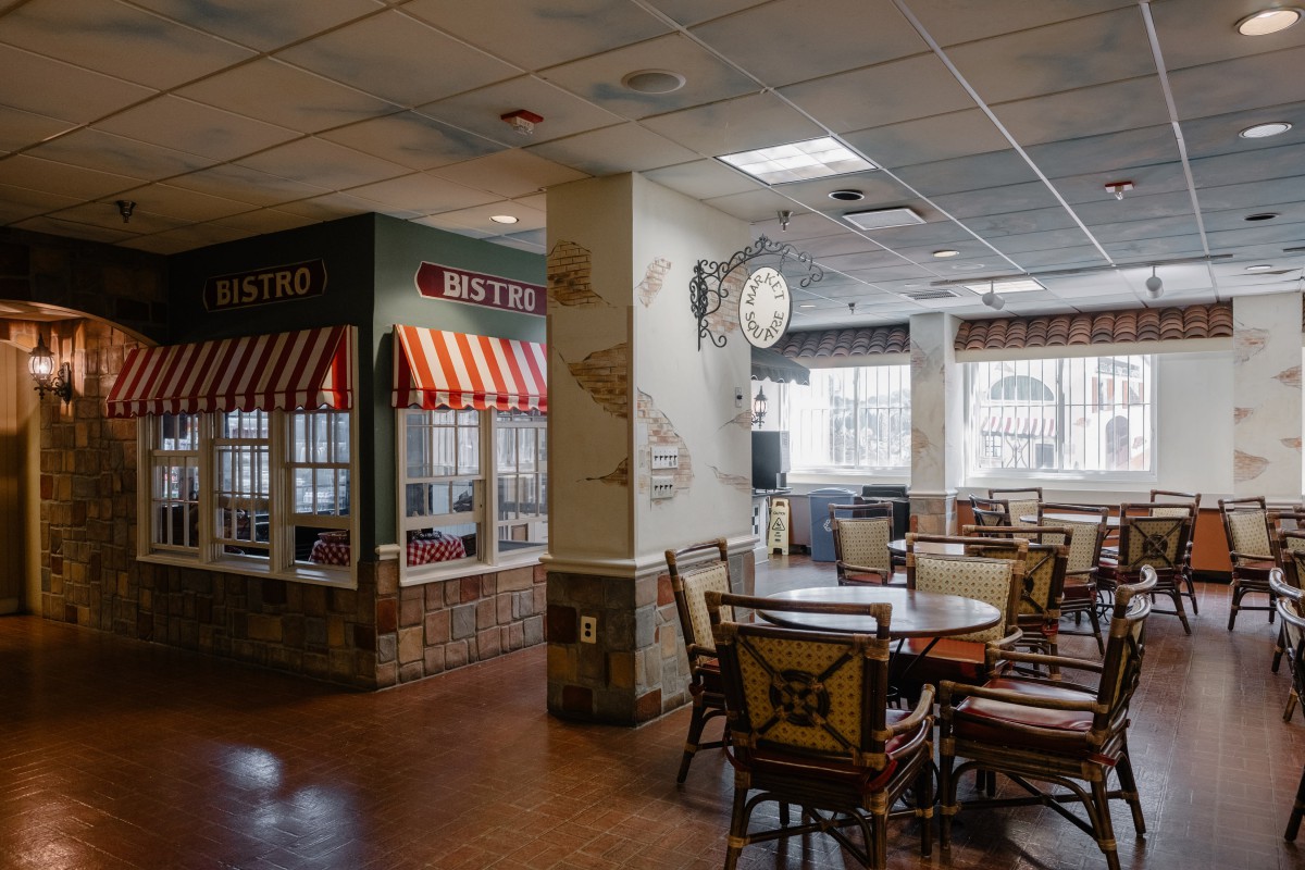 A cozy cafe interior with tables and chairs, featuring large windows and charming decor.