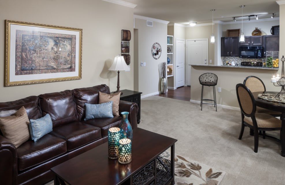 A cozy living room with a leather sofa, coffee table, and open layout leading to the kitchen.