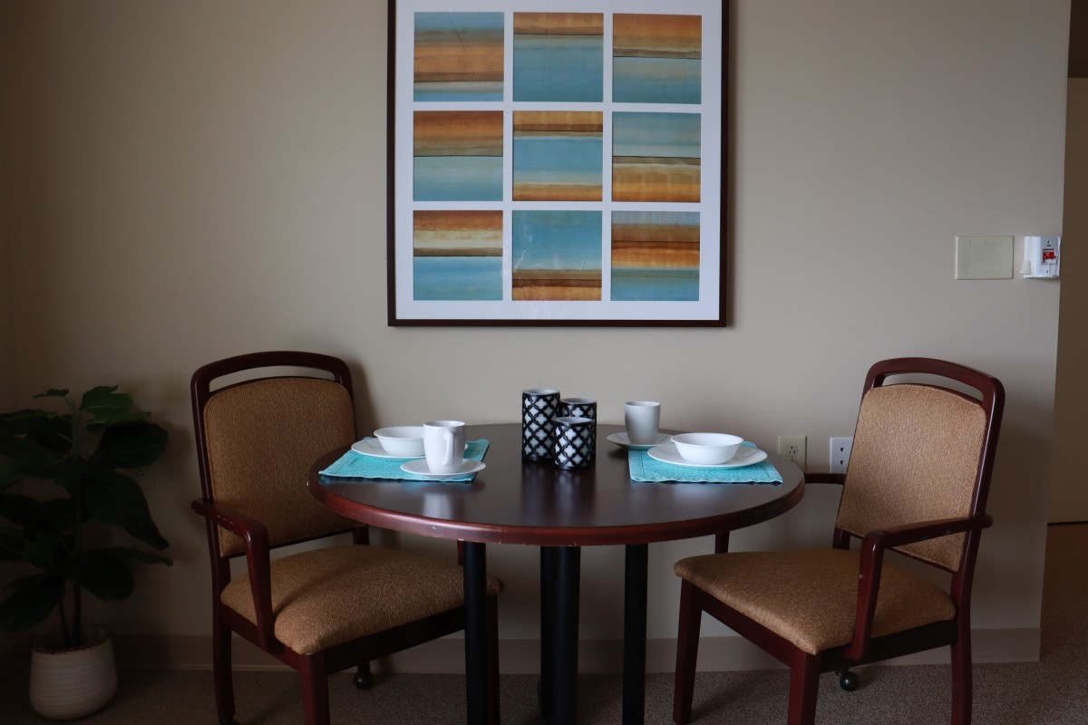 A small dining area with a round table set for two, featuring modern artwork on the wall.