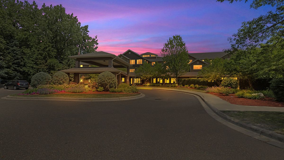 A scenic view of a building at sunset with a driveway and surrounding trees.