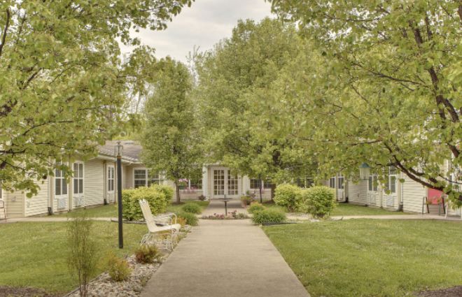 A serene garden pathway surrounded by lush greenery and quaint buildings.