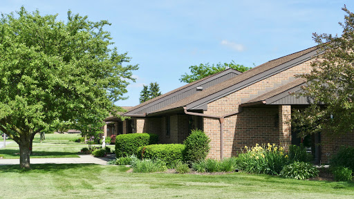 A row of well-kept single-story brick houses surrounded by lush greenery and manicured lawns.