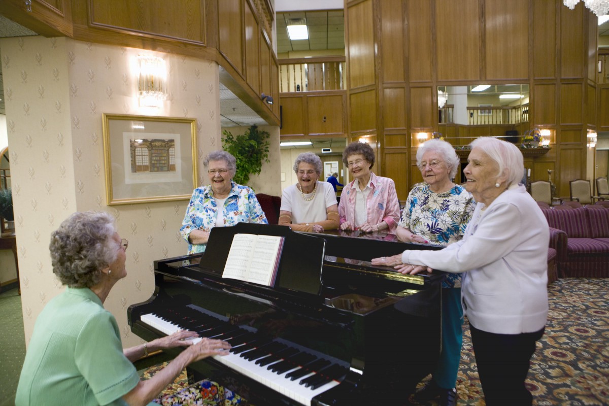A group of elderly individuals gathered around a piano, enjoying a musical moment together indoors.