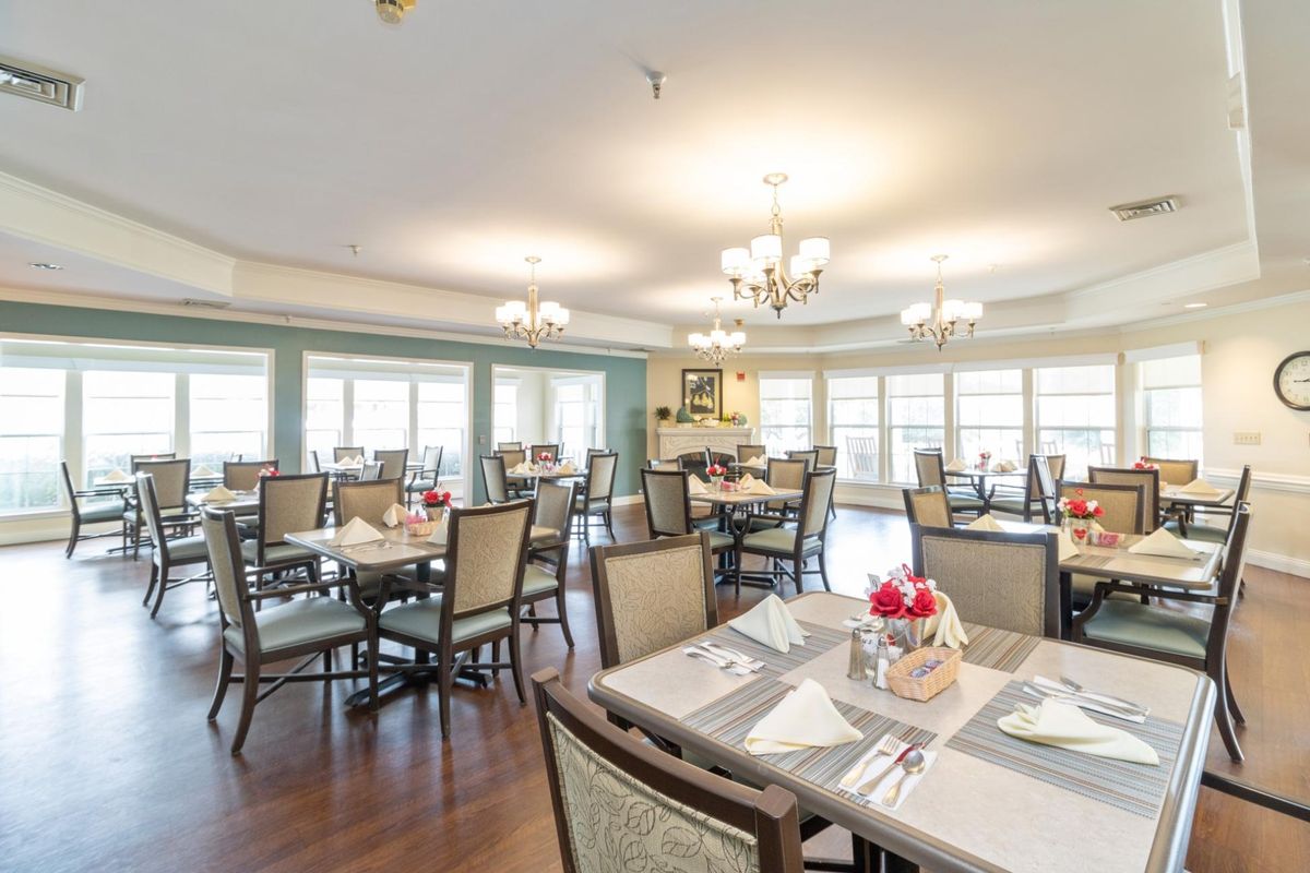 An elegant dining room with neatly arranged tables and chairs, illuminated by chandeliers.