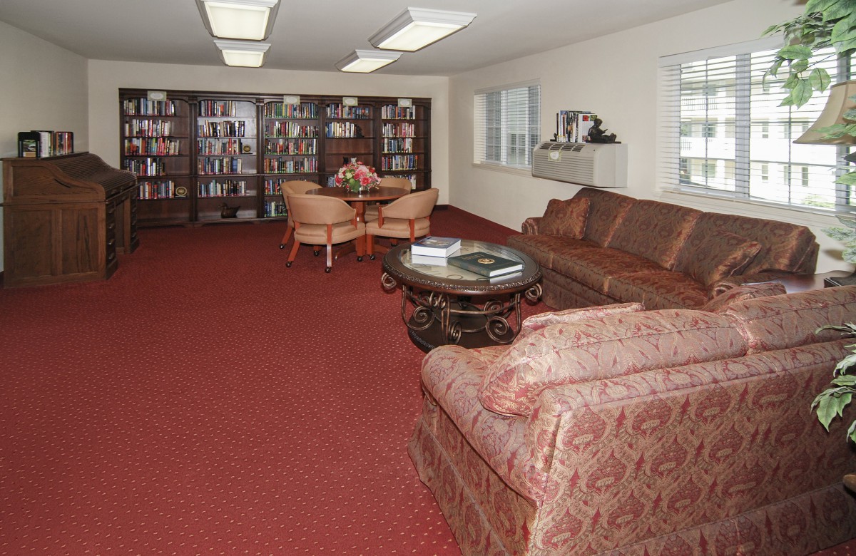A cozy library room with shelves full of books, comfortable seating, and a carpeted floor.