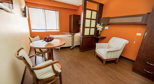 A peaceful and inviting hospital room featuring warm orange walls, a comfortable bed, and seating area with modern furnishings.