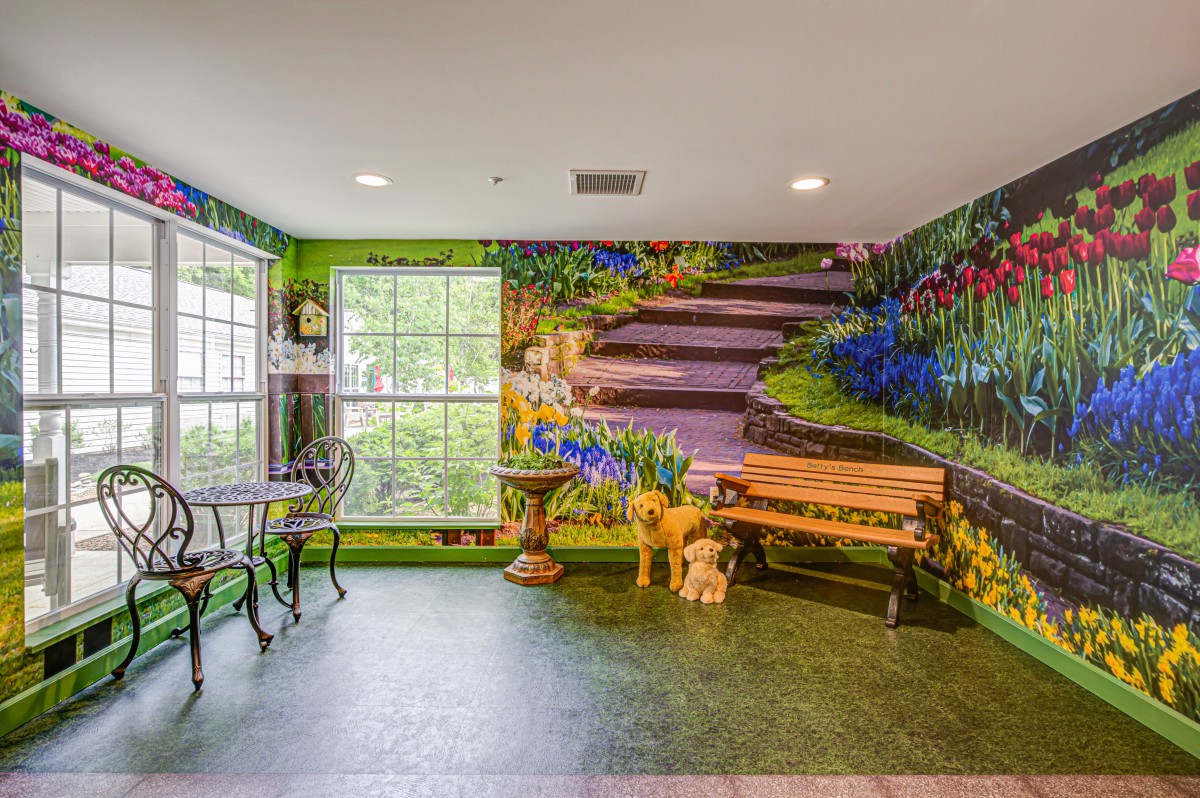 A room with a nature-themed mural featuring a staircase, vibrant flowers, and greenery, along with a small table and chairs by the window.