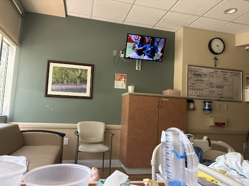 A view of a hospital waiting room with a TV displaying content, comfortable seating, and medical supplies.