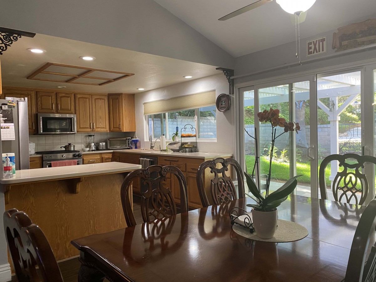 A cozy kitchen and dining area with wooden cabinets and a large dining table, illuminated by natural light from a sliding glass door.