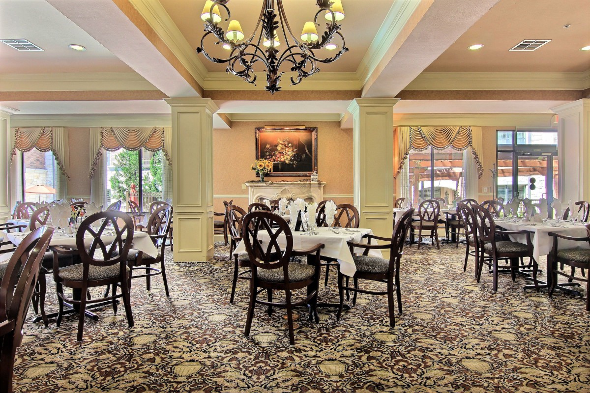 An elegant dining room with neatly arranged tables and chairs, featuring a beautiful chandelier and carpeted flooring.