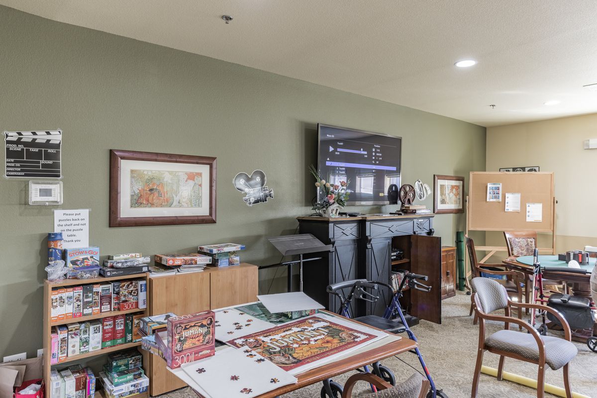A cozy living room featuring shelves with board games, a large television, and various artwork on the walls.