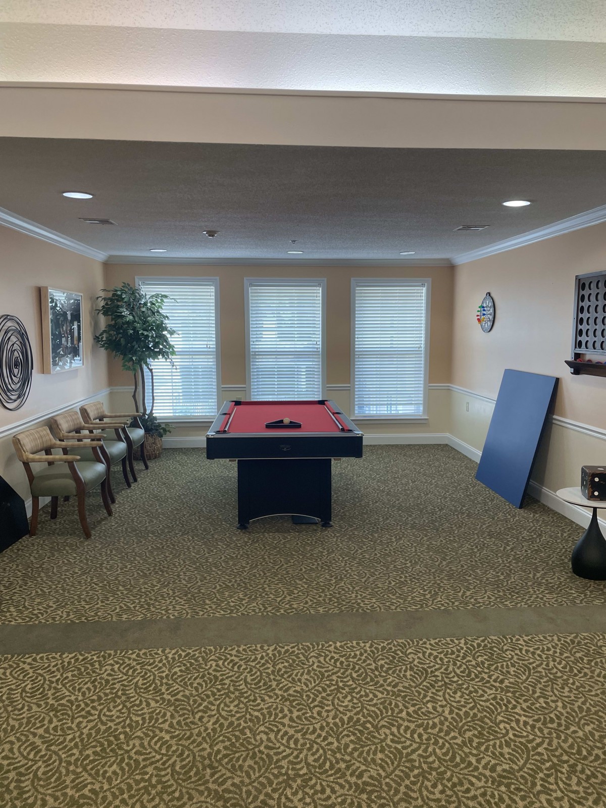 A cozy game room featuring a billiards table surrounded by chairs and large windows.