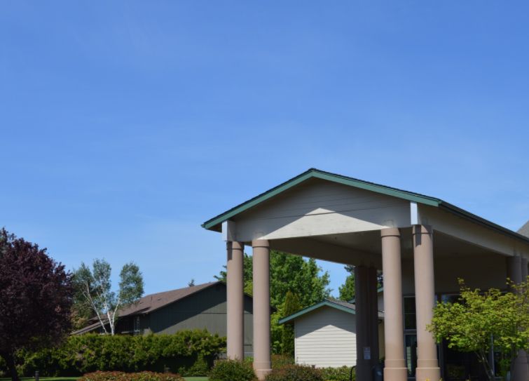 A building with tall columns and a prominent roof structure, set against a clear blue sky with surrounding greenery.