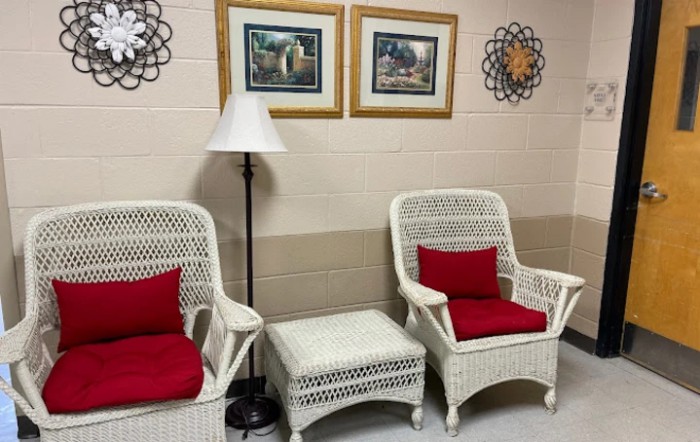 A cozy seating area with wicker chairs and red cushions accompanied by a floor lamp, framed art, and wall decor.