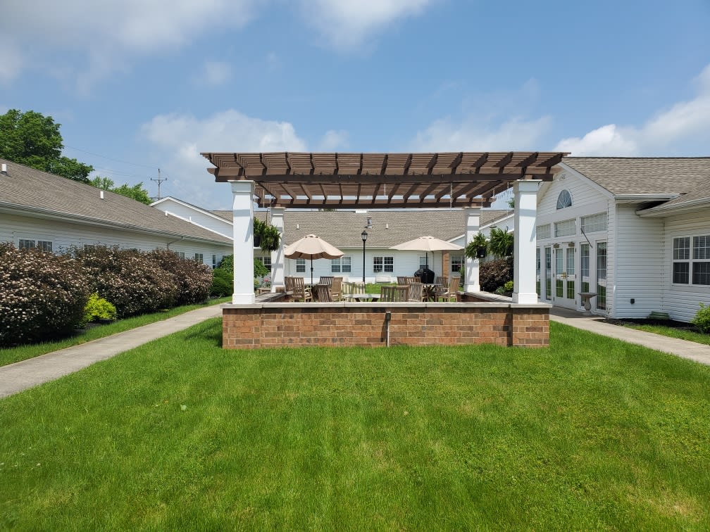 A sunny yard featuring a pergola with patio seating and well-manicured lawn.