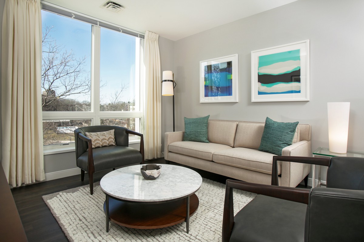 A modern living room with a large window, featuring a sofa, armchairs, a marble coffee table, and contemporary artwork on the walls.