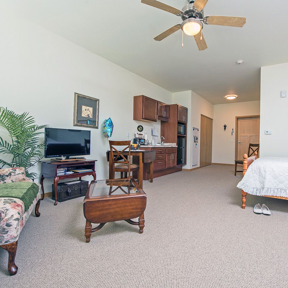 A cozy living area with a kitchenette, featuring a sofa, TV, table, and ceiling fan.